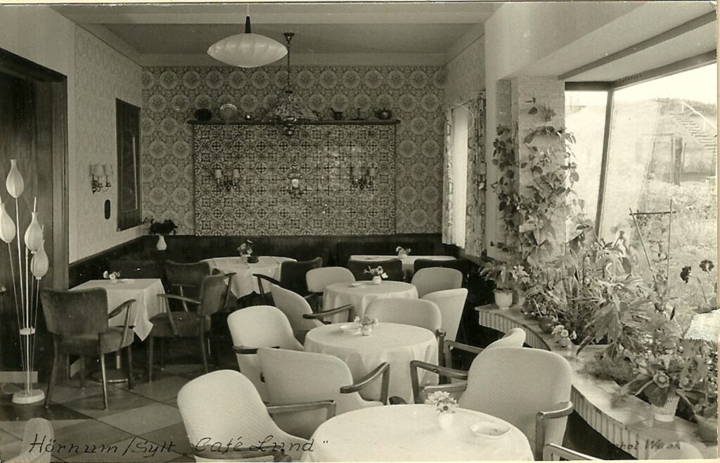 Ein altes Foto eines Restaurants mit Tischen und Stühlen, das die Rubrik „Über uns“ repräsentiert.